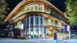 A two-story building with a curved facade, large windows, and a balcony with a railing. - D'S CASA Hotel (Dharamshala)
