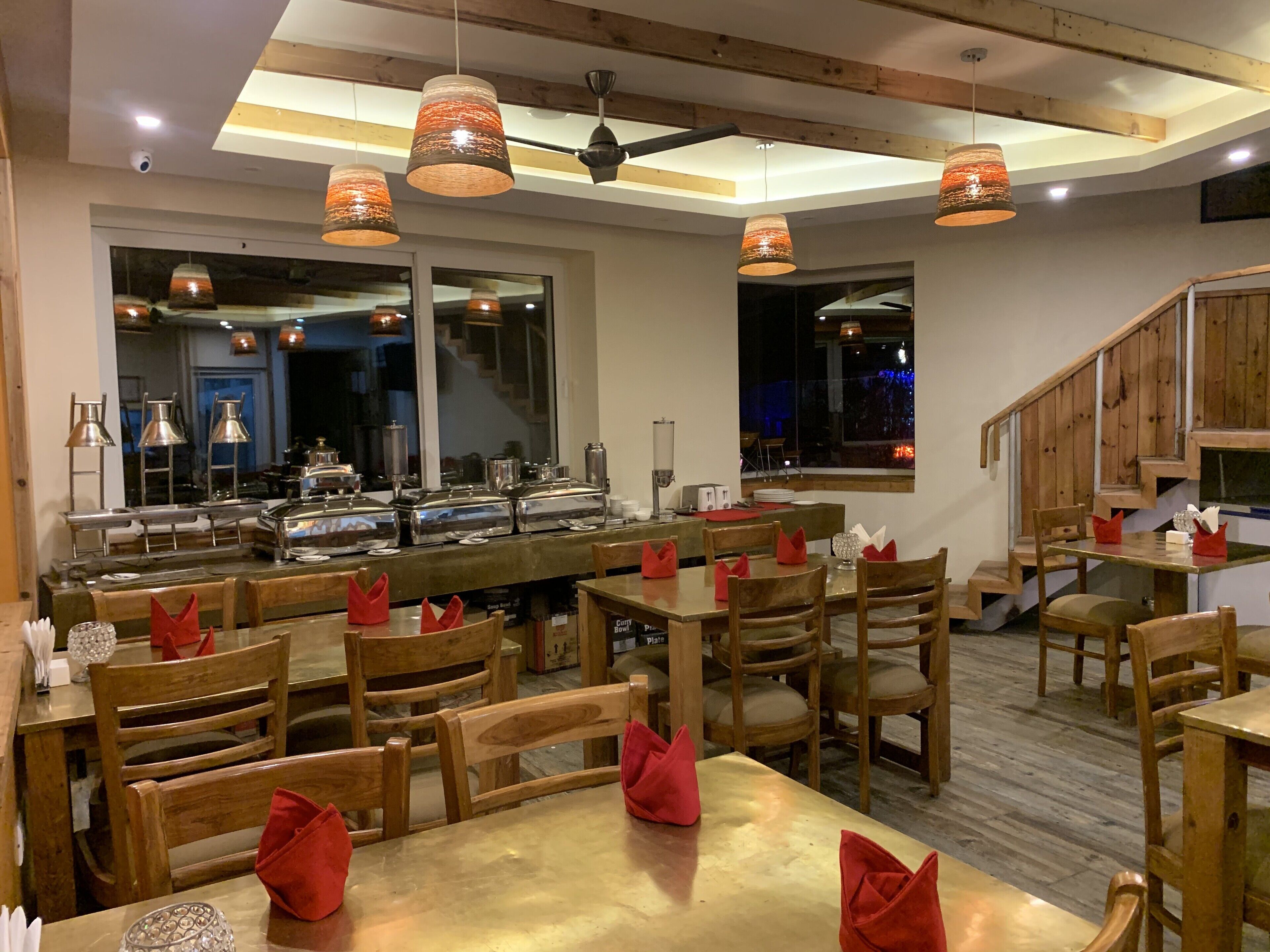 A restaurant with wooden tables and chairs, red napkins, and pendant lights.