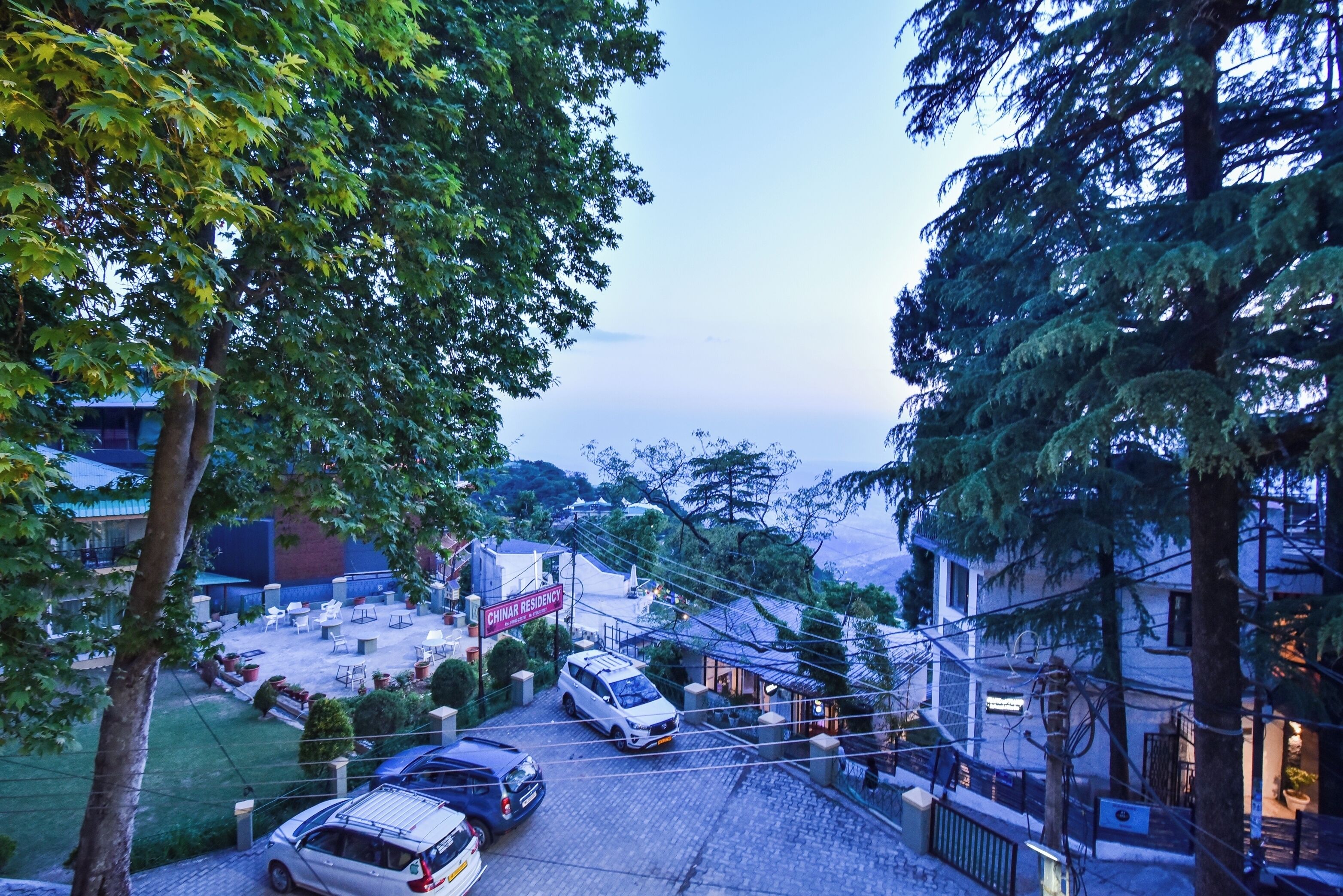 Un barrio residencial con entrada pavimentada, automóviles estacionados y un edificio que dice "CHINAR RESIDENCY".