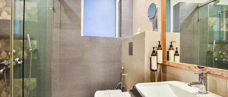 A modern bathroom with a glass shower enclosure, a toilet, a sink with a mirror, and a small window.