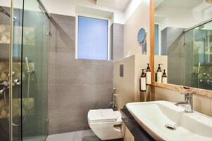 A modern bathroom with a glass shower enclosure, a toilet, a sink with a mirror, and a small window.