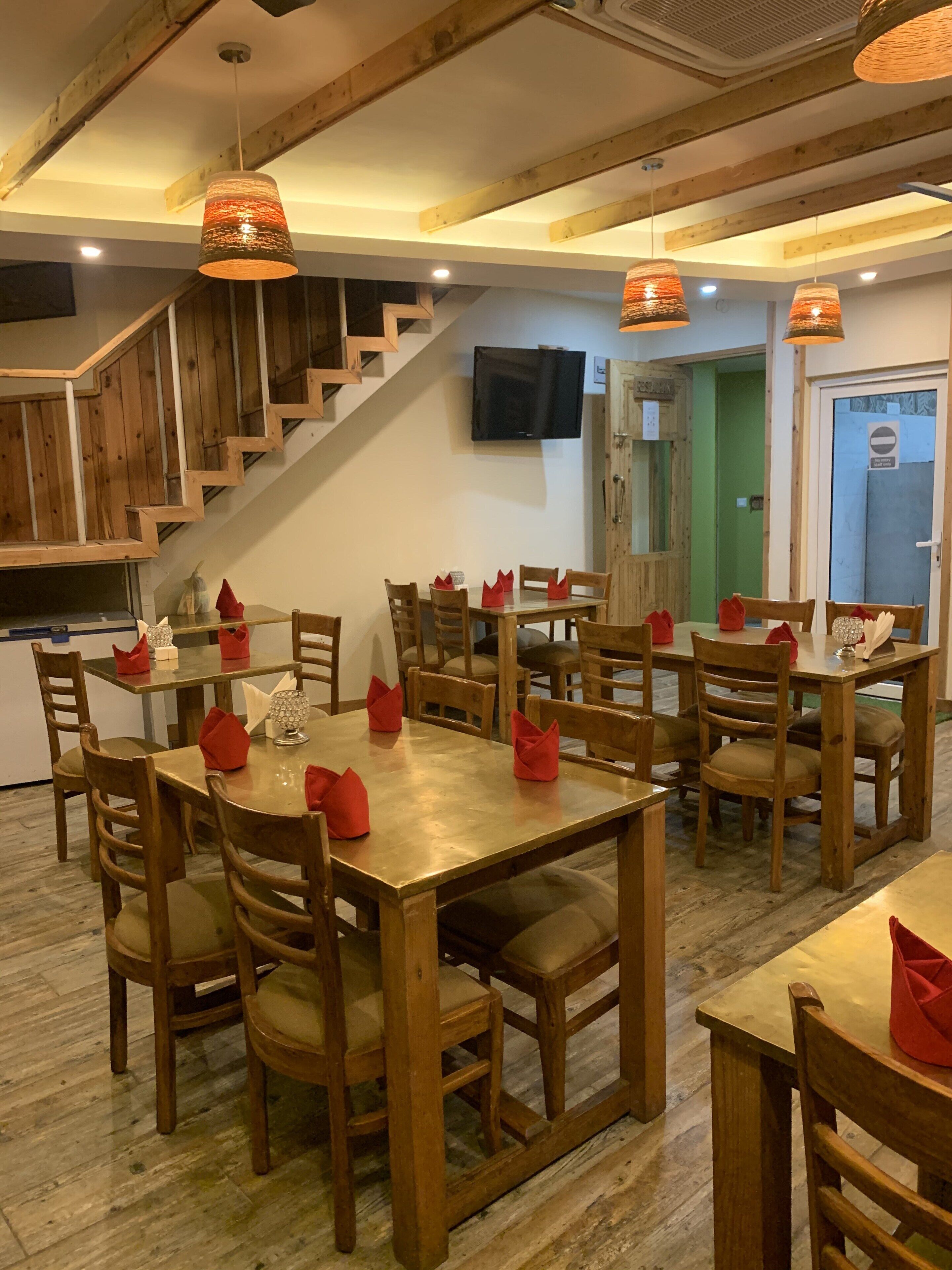 A dining area with wooden tables and chairs, red napkins, and hanging pendant lights.