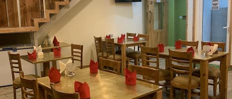 Un comedor con mesas y sillas de madera, servilletas rojas y lámparas colgantes.