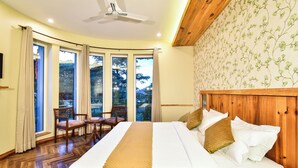 A hotel room with a large bed, wooden headboard, and a view of trees through the windows. - D'S CASA Hotel (Dharamshala)