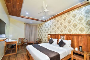 Habitación de hotel con techo de madera, cama con almohadas blancas y oscuras, escritorio con lámpara y una silla.