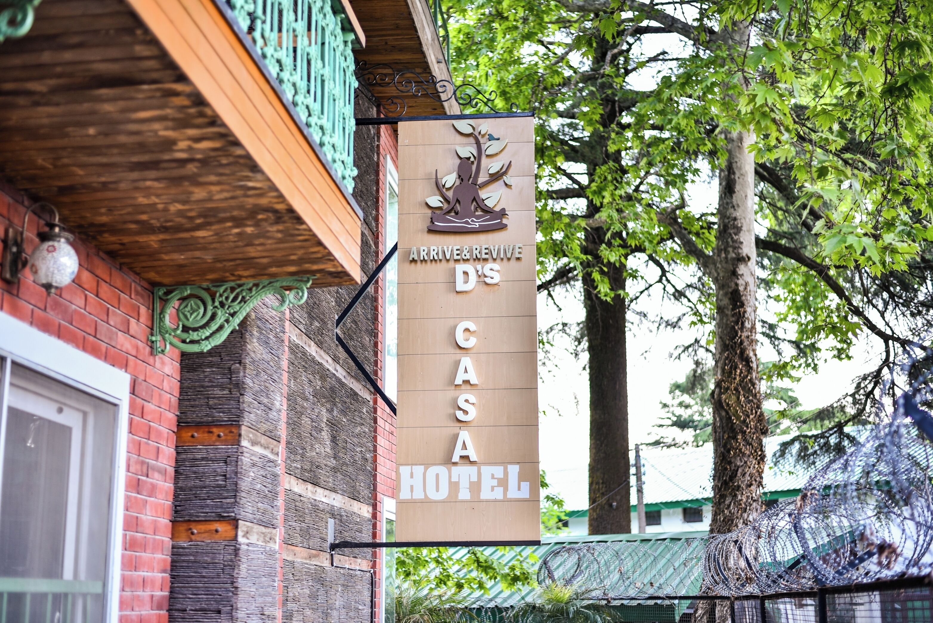 A sign for the Arrive & Revive D'S Casa Hotel, featuring a logo with a tree and a person meditating.