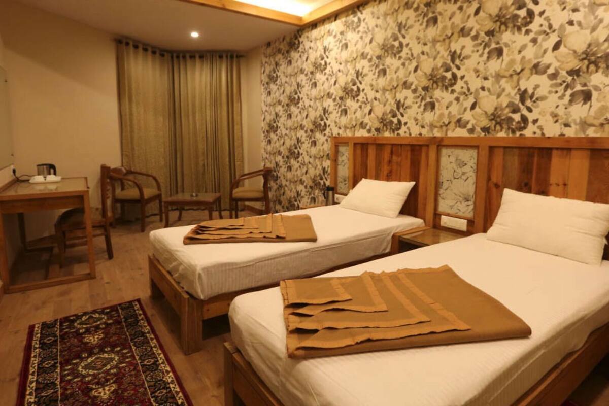 A hotel room with two beds, a desk, chairs, a telephone, and a patterned wall.