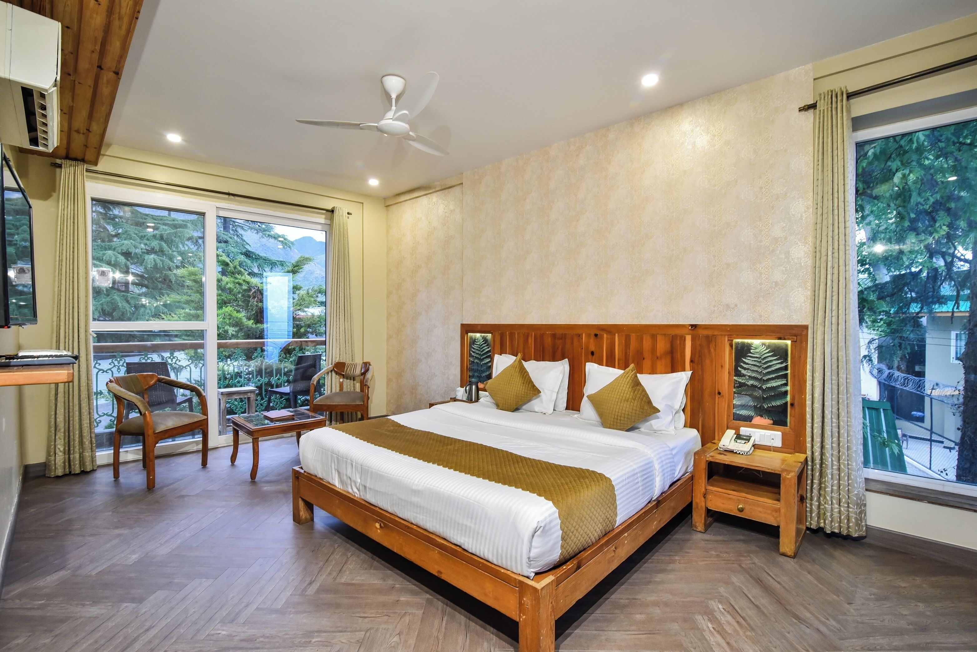A bedroom with a wooden bed, a nightstand, a chair, a desk, and a large window with a view of greenery.