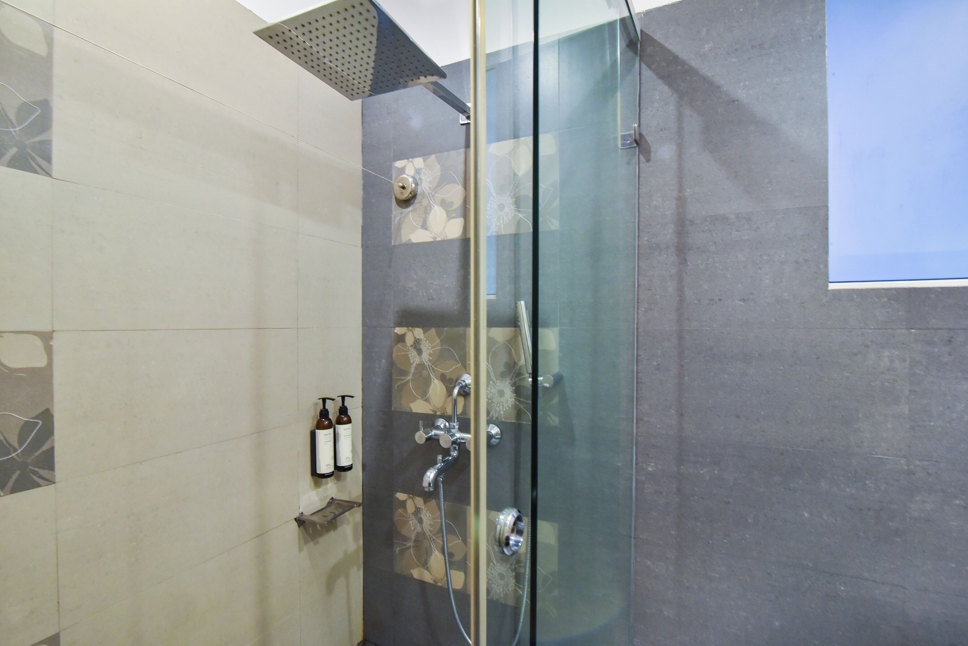 A modern bathroom with a glass-enclosed shower, tiled walls, and a small shelf with toiletries.