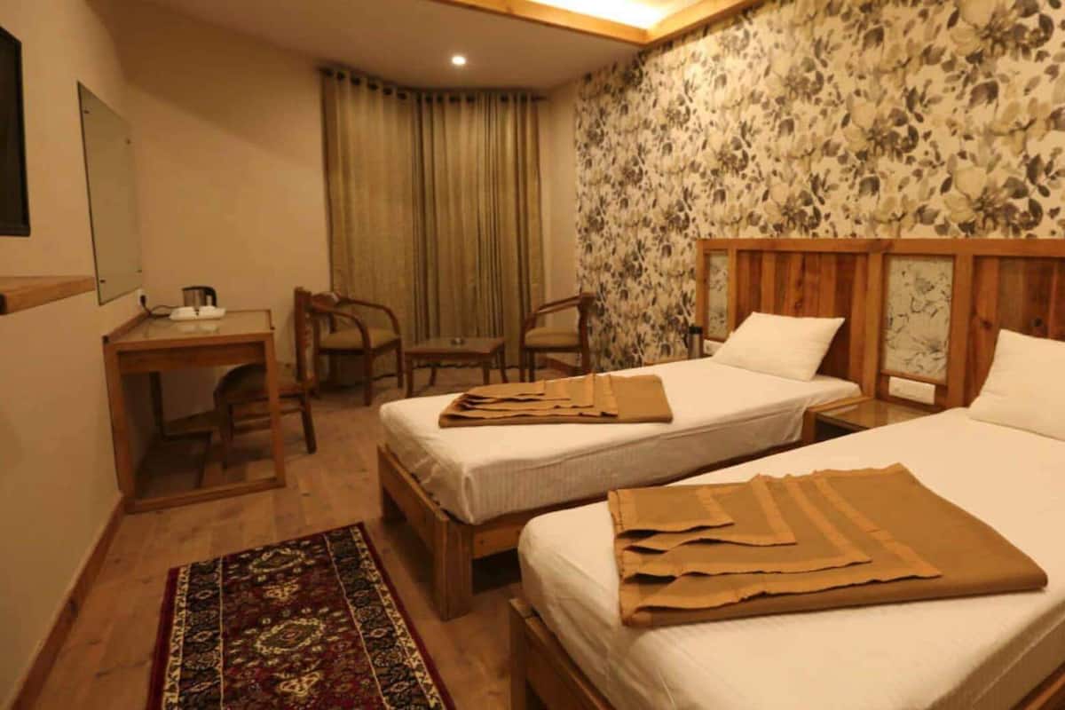 A hotel room with two beds, a desk, chairs, a telephone, and a floral wallpaper.