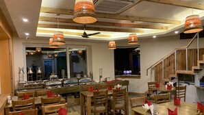A restaurant with wooden tables and chairs, a bar area with various appliances, and pendant lighting. - D'S CASA Hotel (Dharamshala)