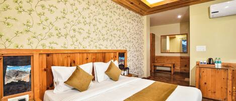 A neatly arranged hotel room with a large bed, wooden headboard, a bedside table with a phone, and a mirror on the wall.