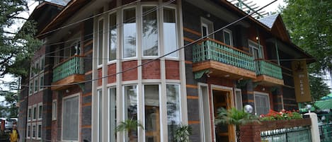 Un edificio de dos pisos con fachada curva, ventanas grandes y un balcón con barandillas verdes.