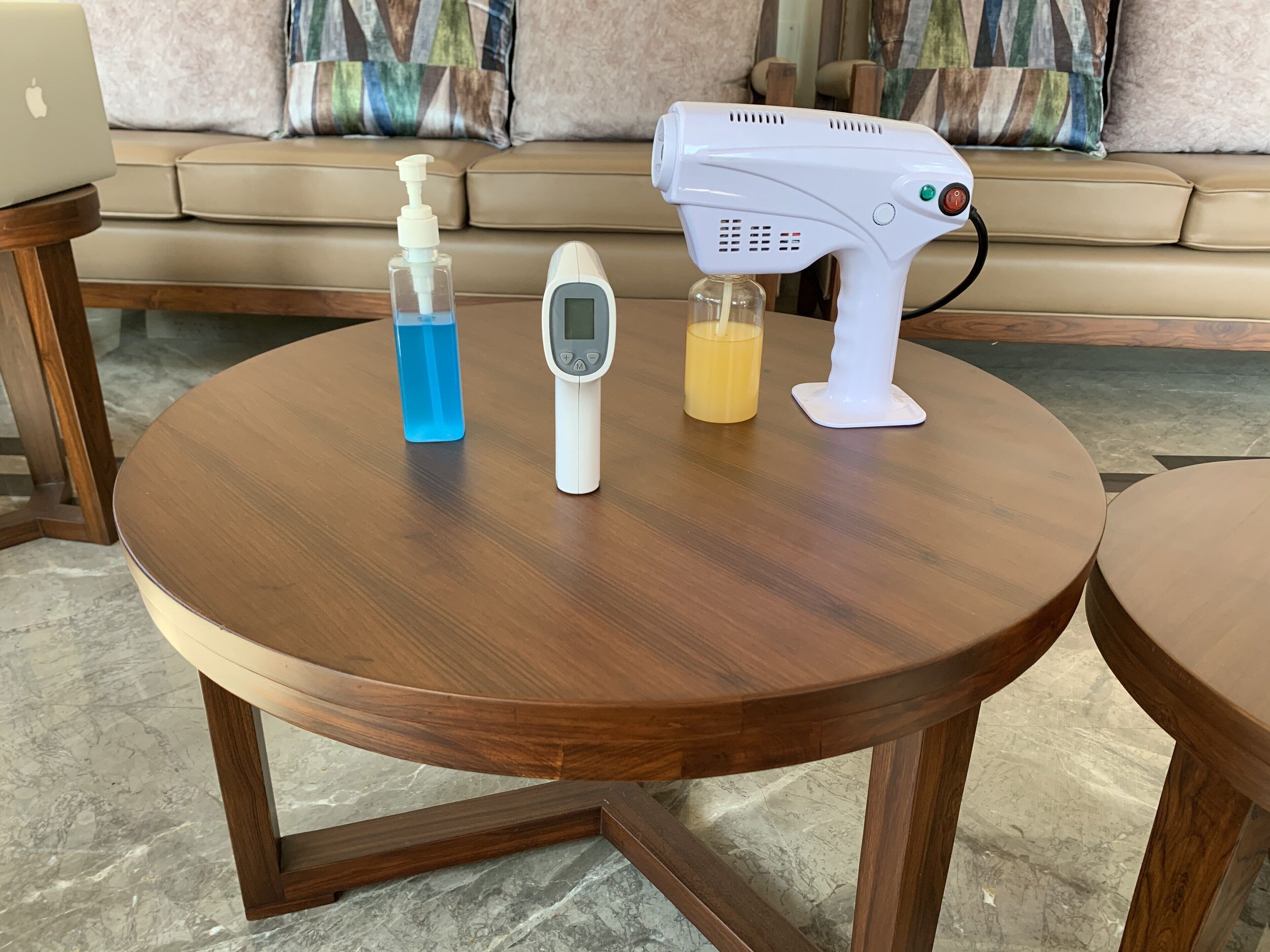 Una mesa redonda de madera con una computadora portátil, un dispensador de gel antibacterial, un termómetro digital y un secador de pelo.