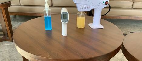 Een ronde houten tafel met een laptop, een fles handdesinfectiemiddel, een digitaal thermometer en een haardroger.