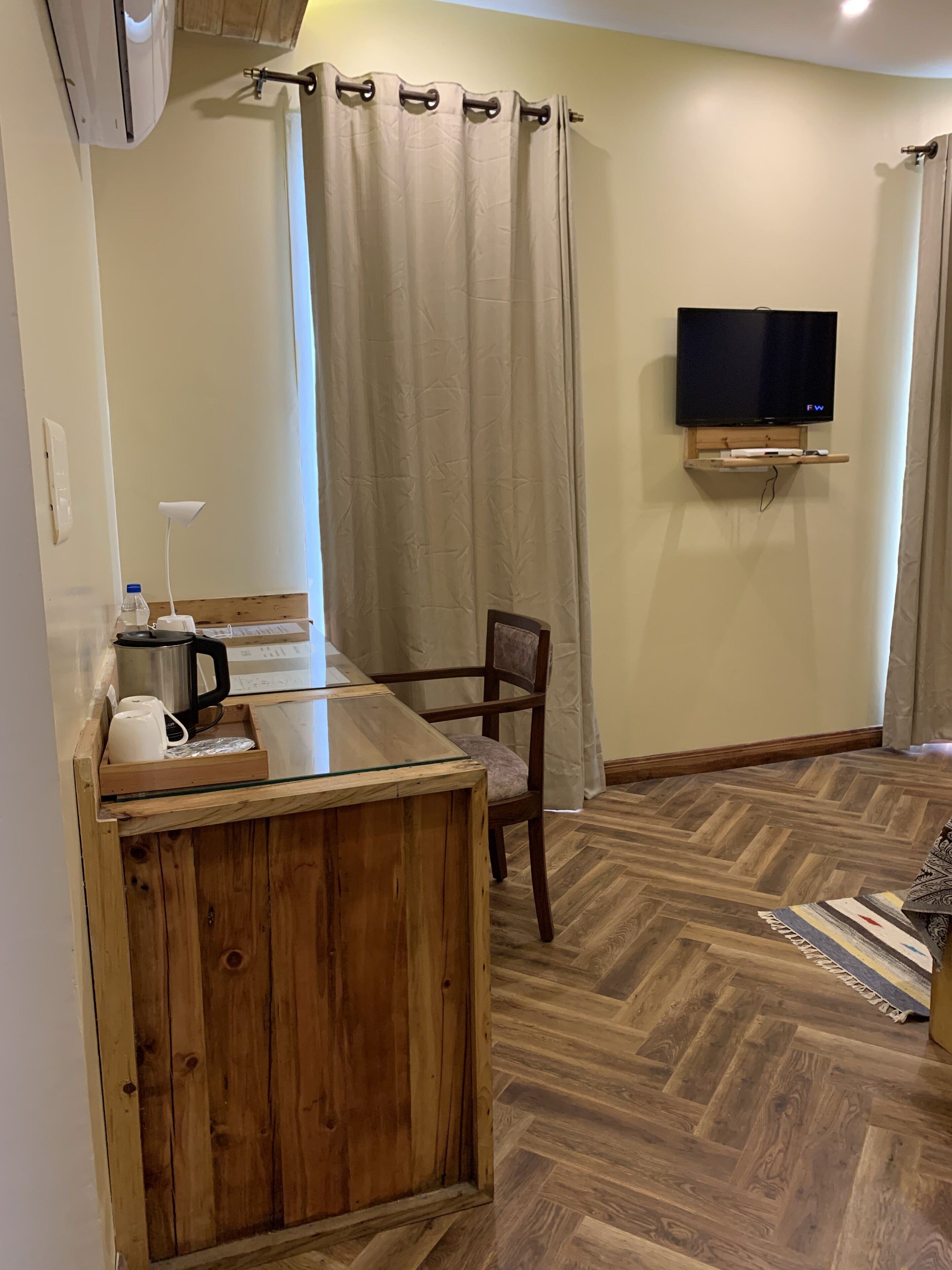 A compact living space with a wooden counter, a chair, a television mounted on the wall, and a herringbone-patterned floor.