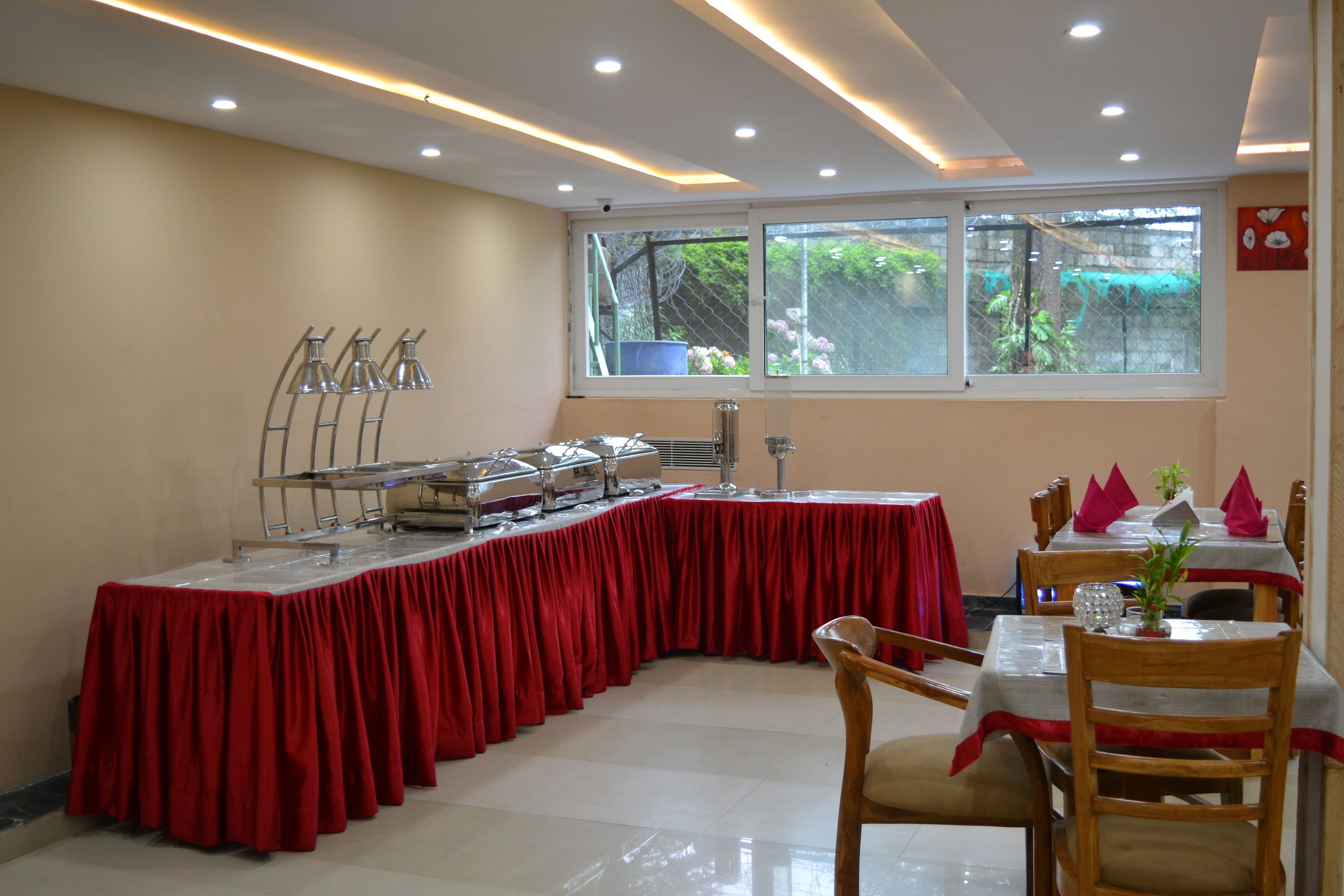 A dining area with a long table covered in a red tablecloth, surrounded by wooden chairs.