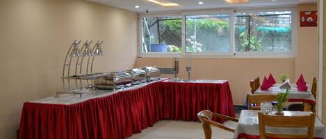 A dining area with a long table covered in a red tablecloth, surrounded by wooden chairs.