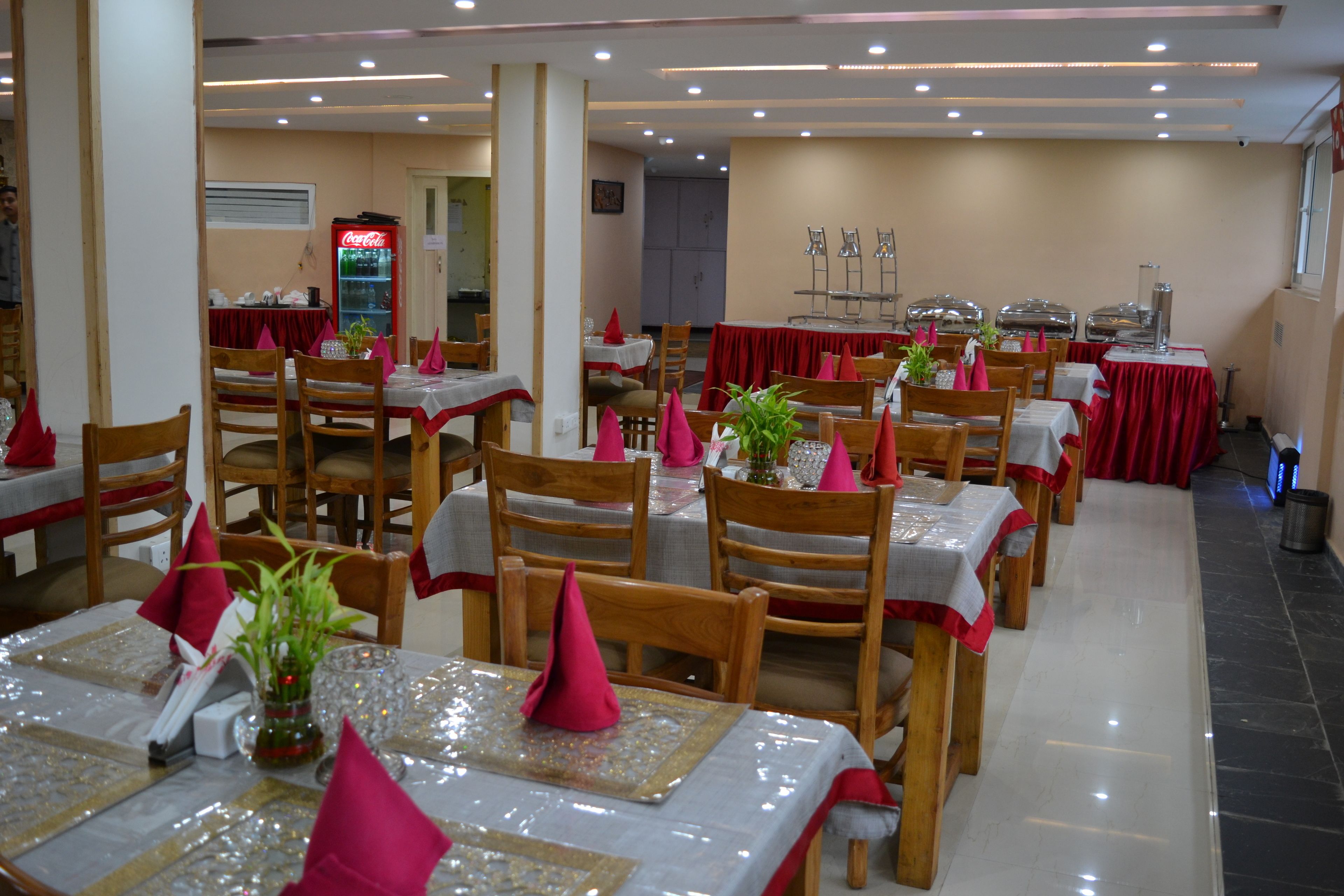 A dining area with multiple tables, each set with wooden chairs, red tablecloths, and pink napkins.