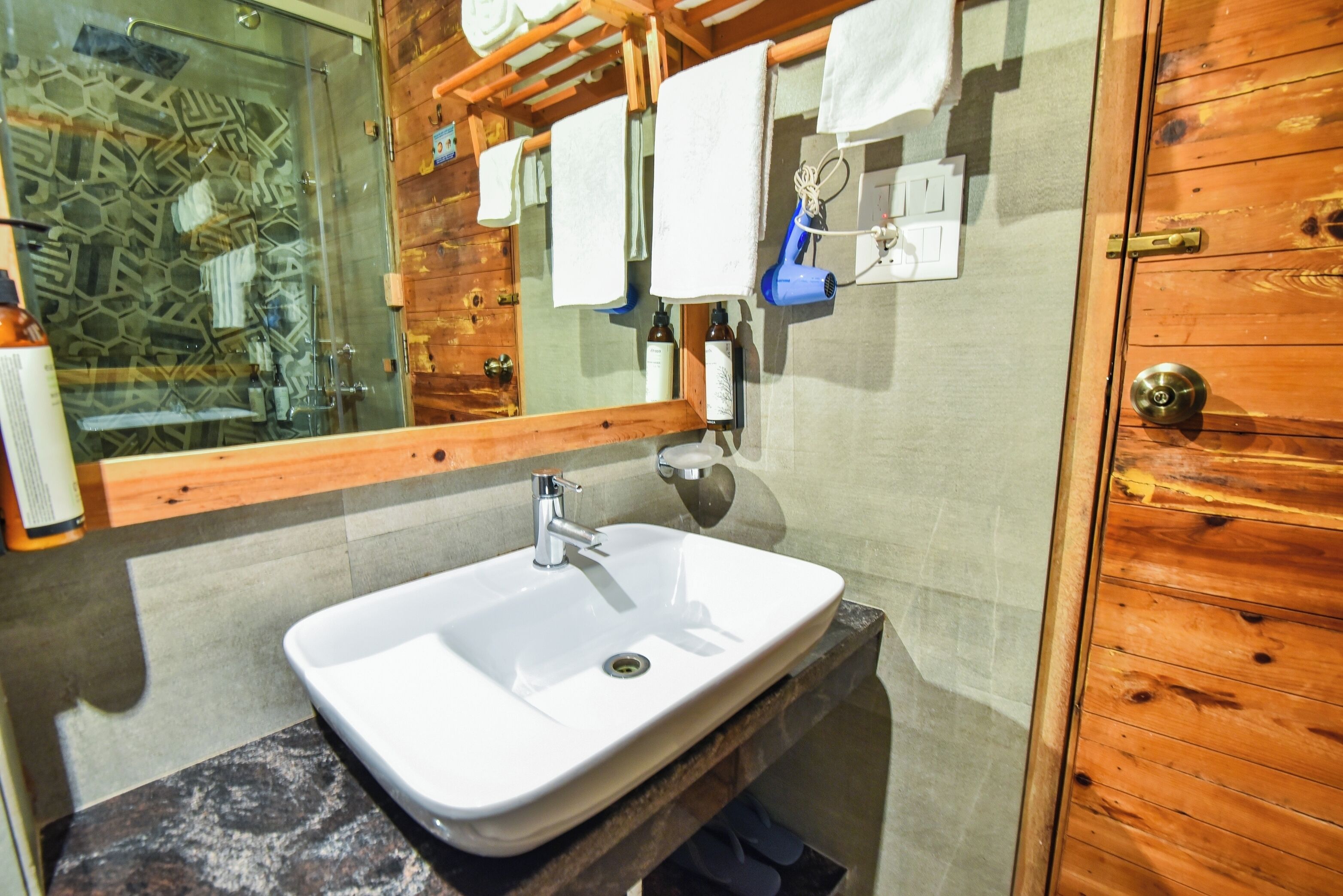 A bathroom with a white sink, wooden walls, a glass shower enclosure, and a towel rack with white towels.