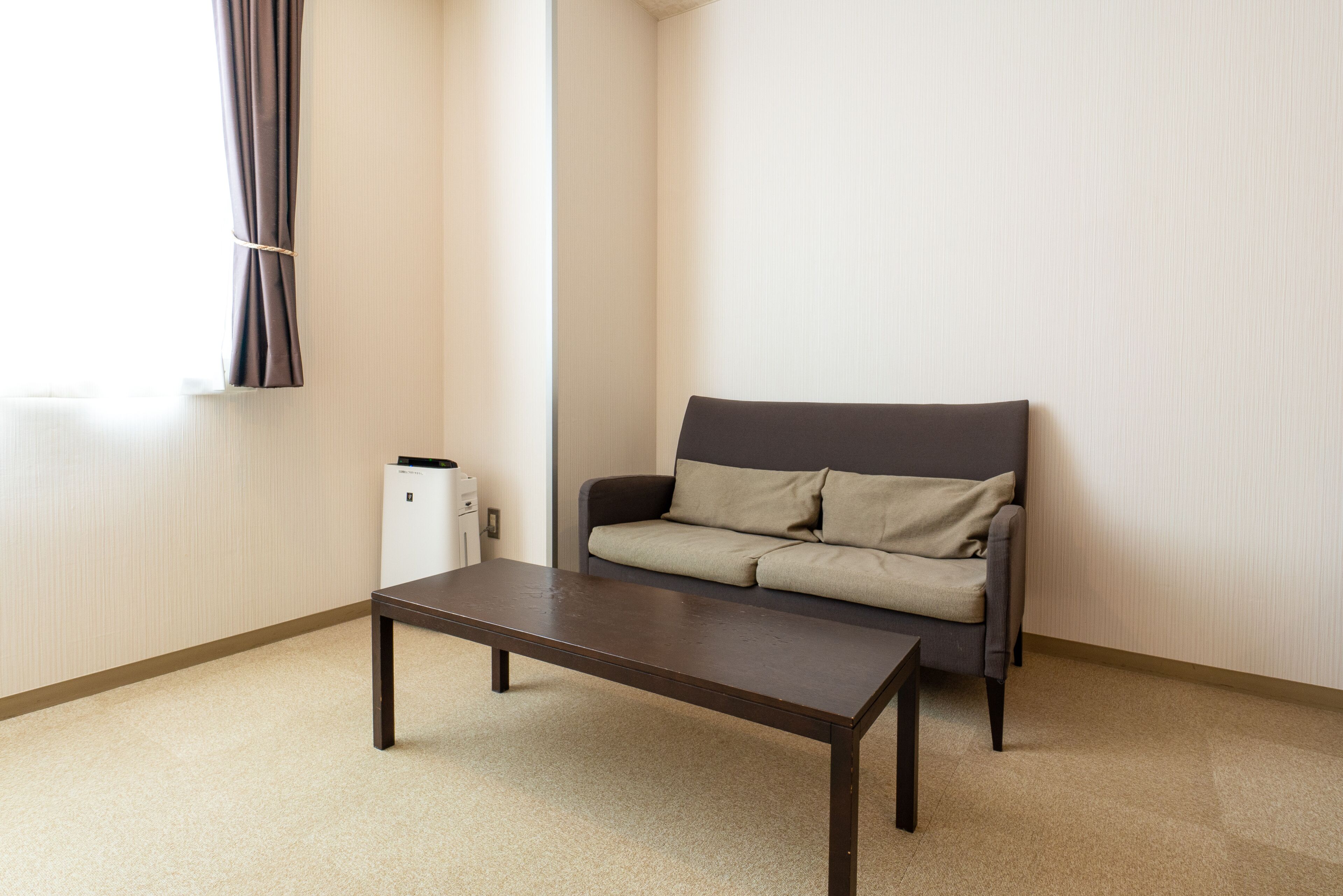 A room with a dark brown table, a grey sofa with beige cushions, and a white radiator.