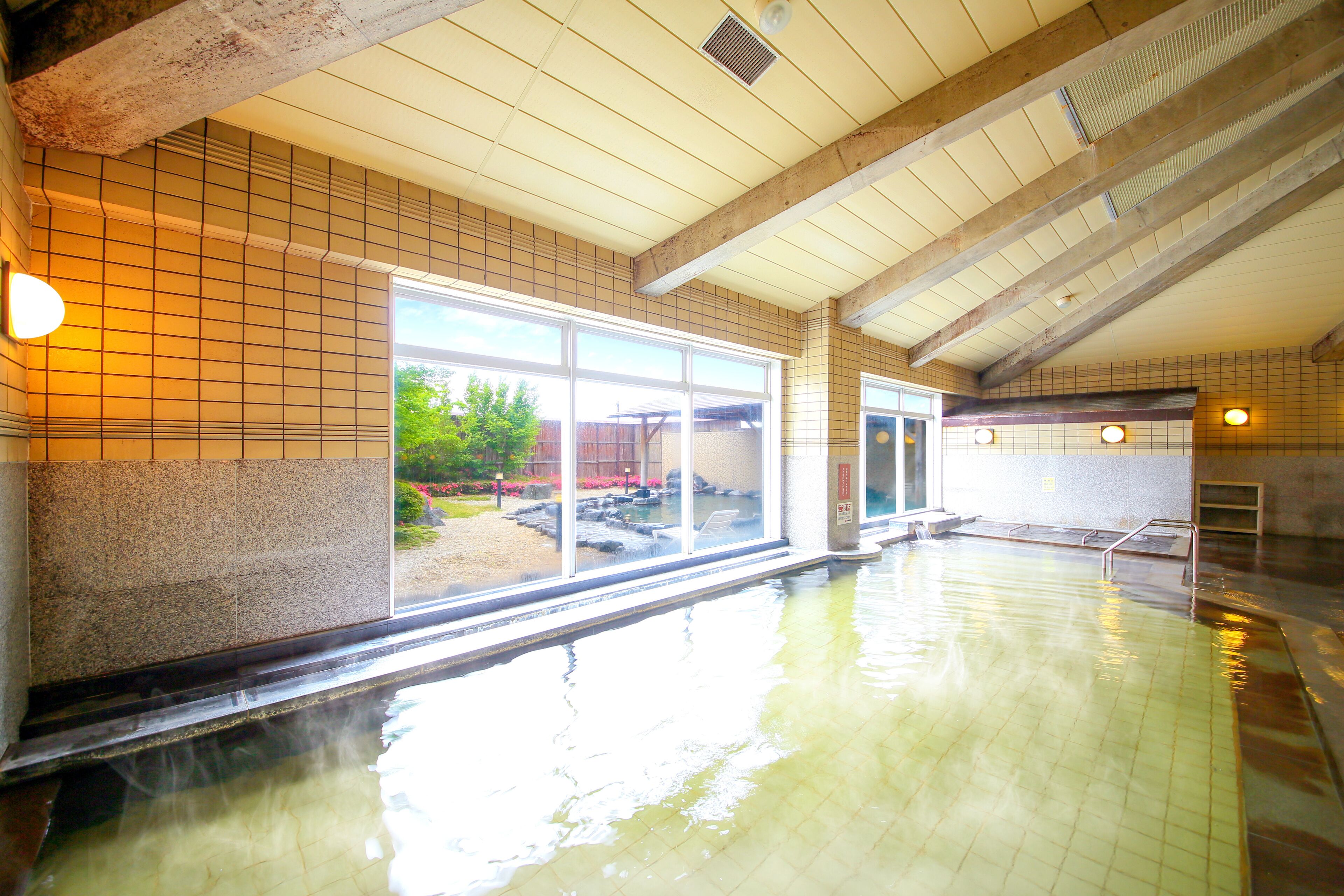 Ein großes Hallenbad mit gefliesten Wänden und Blick auf einen angelegten Garten.