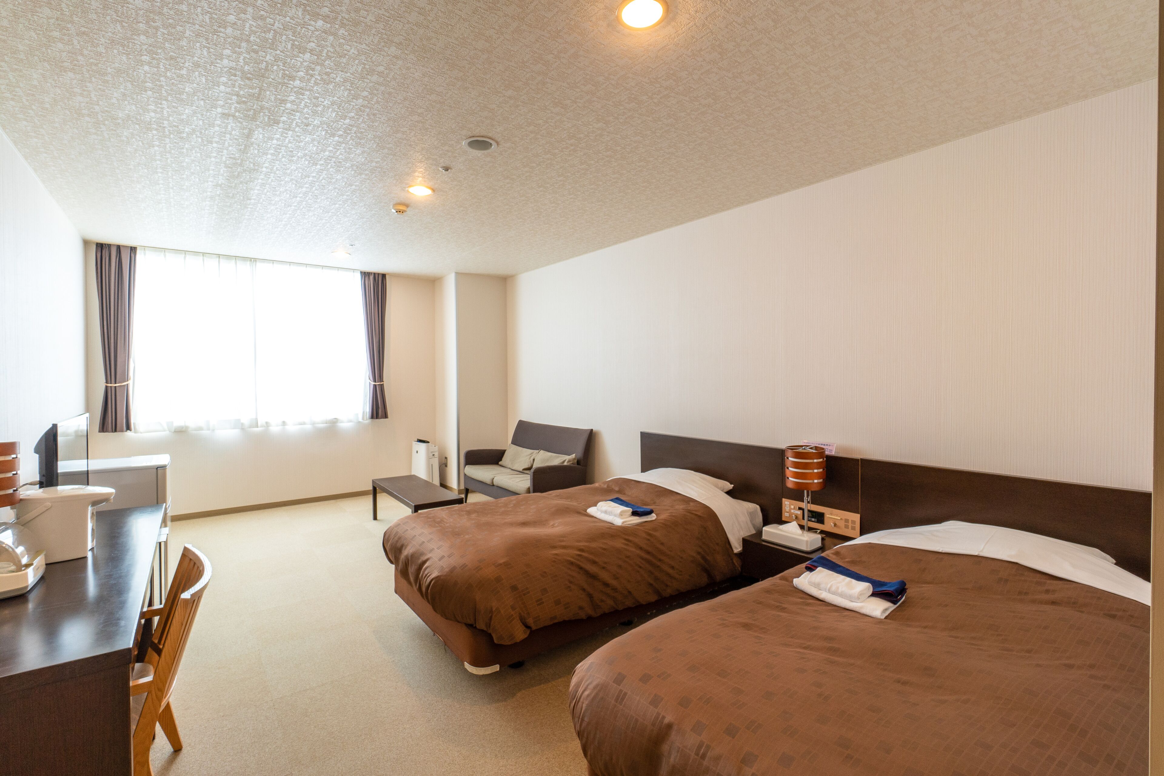 A hotel room with two beds, a desk, a chair, and a window with curtains.