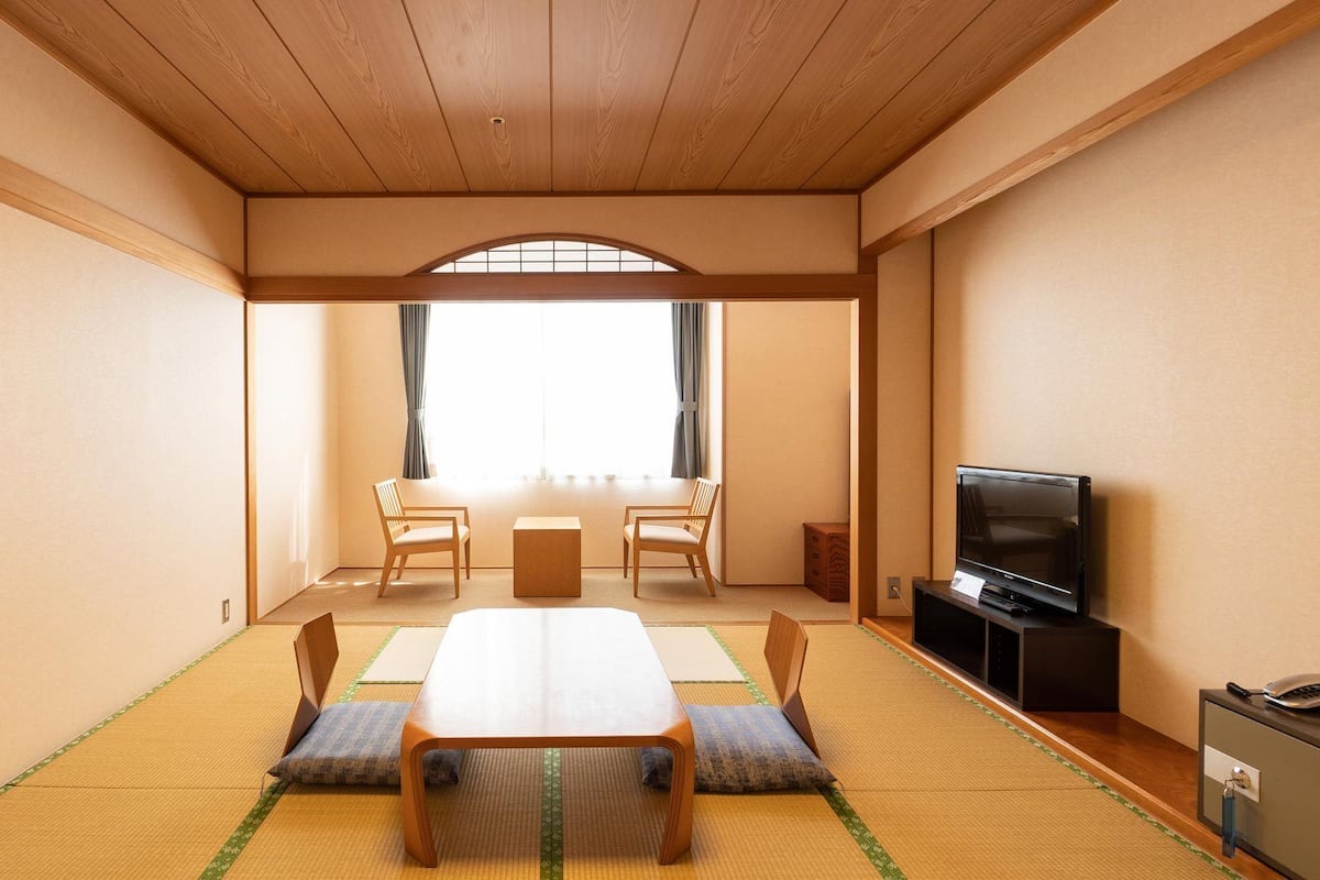 Une pièce de style japonais traditionnel, avec un sol recouvert de tatamis, une table basse, des chaises, un téléviseur et un meuble.