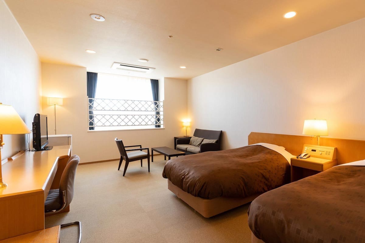 Une chambre d’hôtel avec deux lits, un bureau, une chaise, une petite table et une fenêtre avec des rideaux.