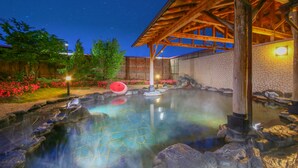 Un área de aguas termales con una estructura de madera, muros de piedra y un cielo nocturno despejado.