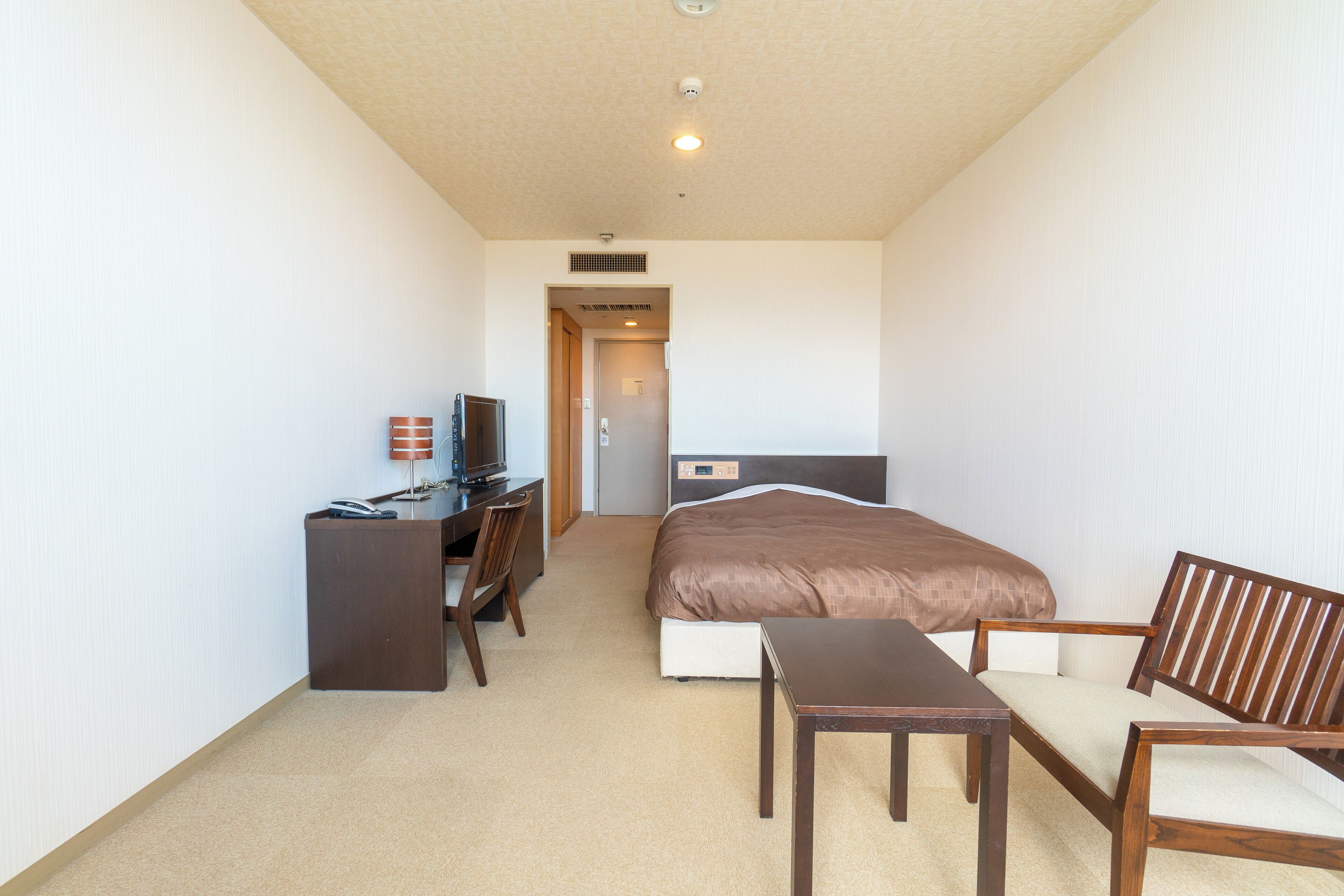 A hotel room with a bed, a desk with a chair, a television, and a small table.