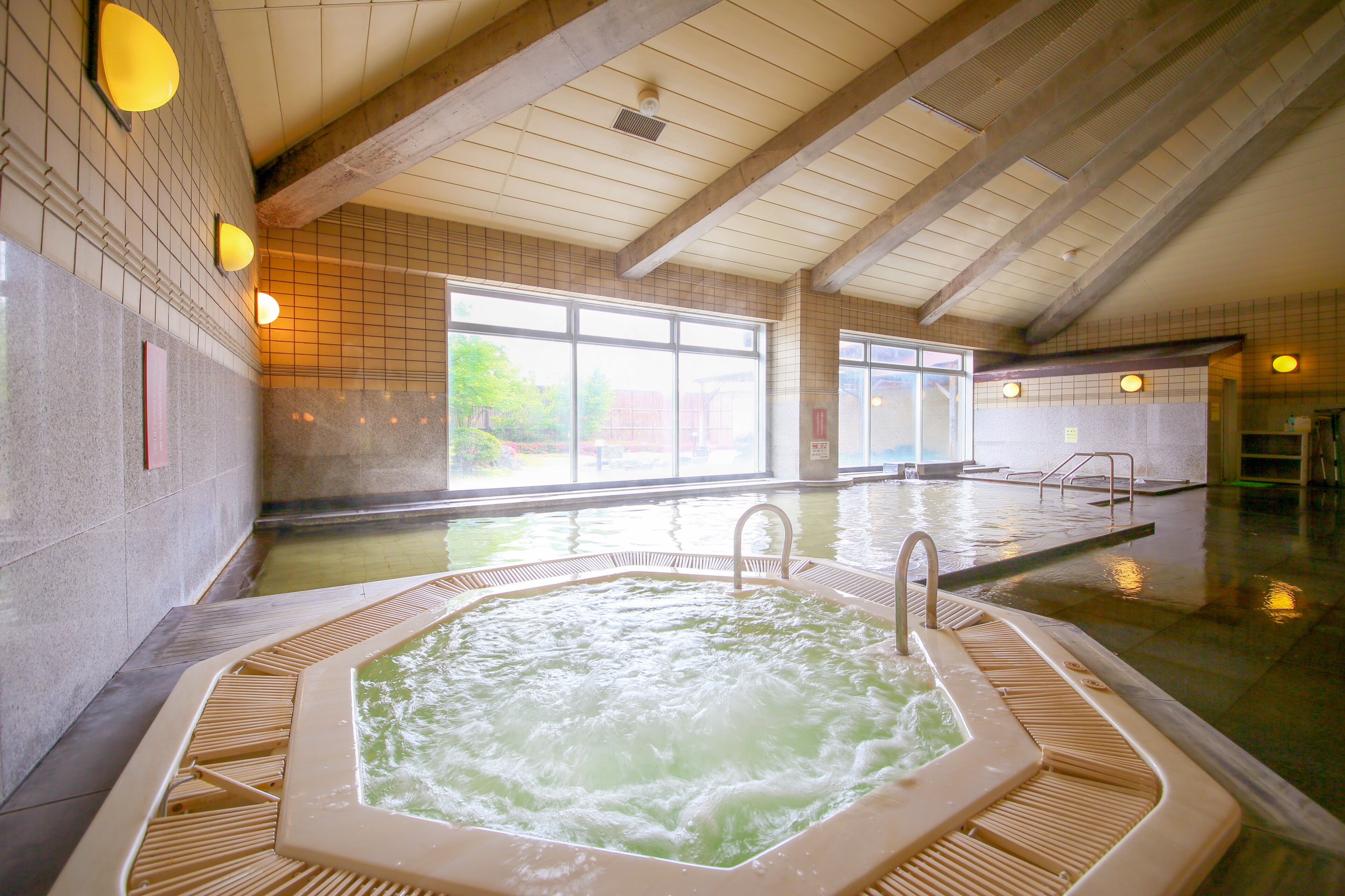 A large indoor swimming pool with a hot tub, wooden beams, and large windows.