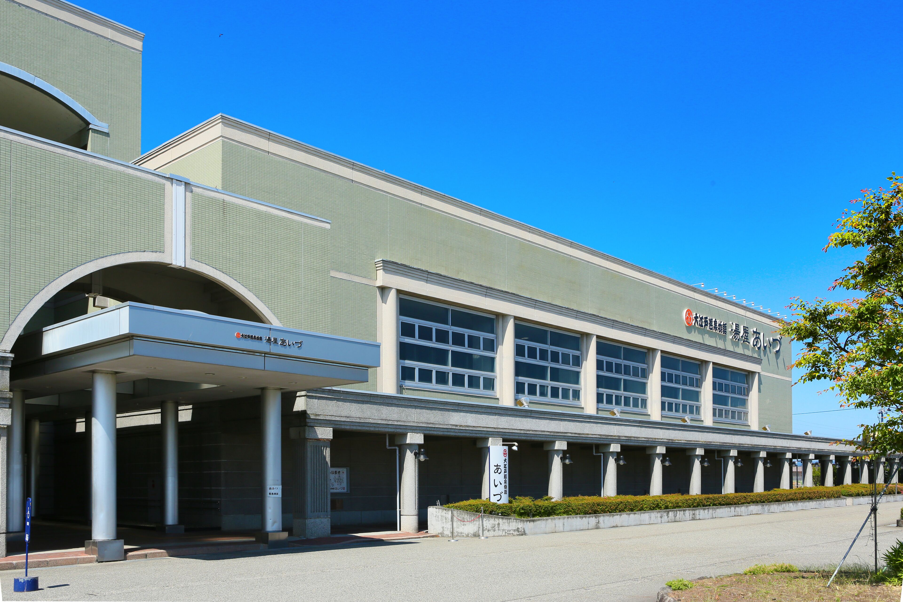 A modern building with a covered entrance, large windows, and a sign in a foreign language.