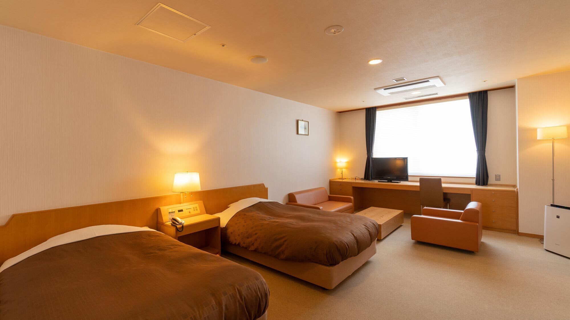 Una habitación de hotel con dos camas, un escritorio, una silla, un televisor y una lámpara.