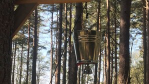 Een metalen emmer hangt aan een houten constructie in een bos.