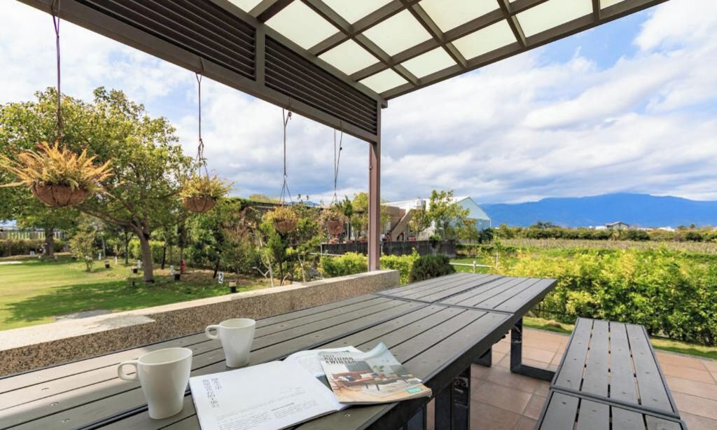 An outdoor seating area with a table, chairs, hanging planters, and a view of a landscaped garden and mountains.