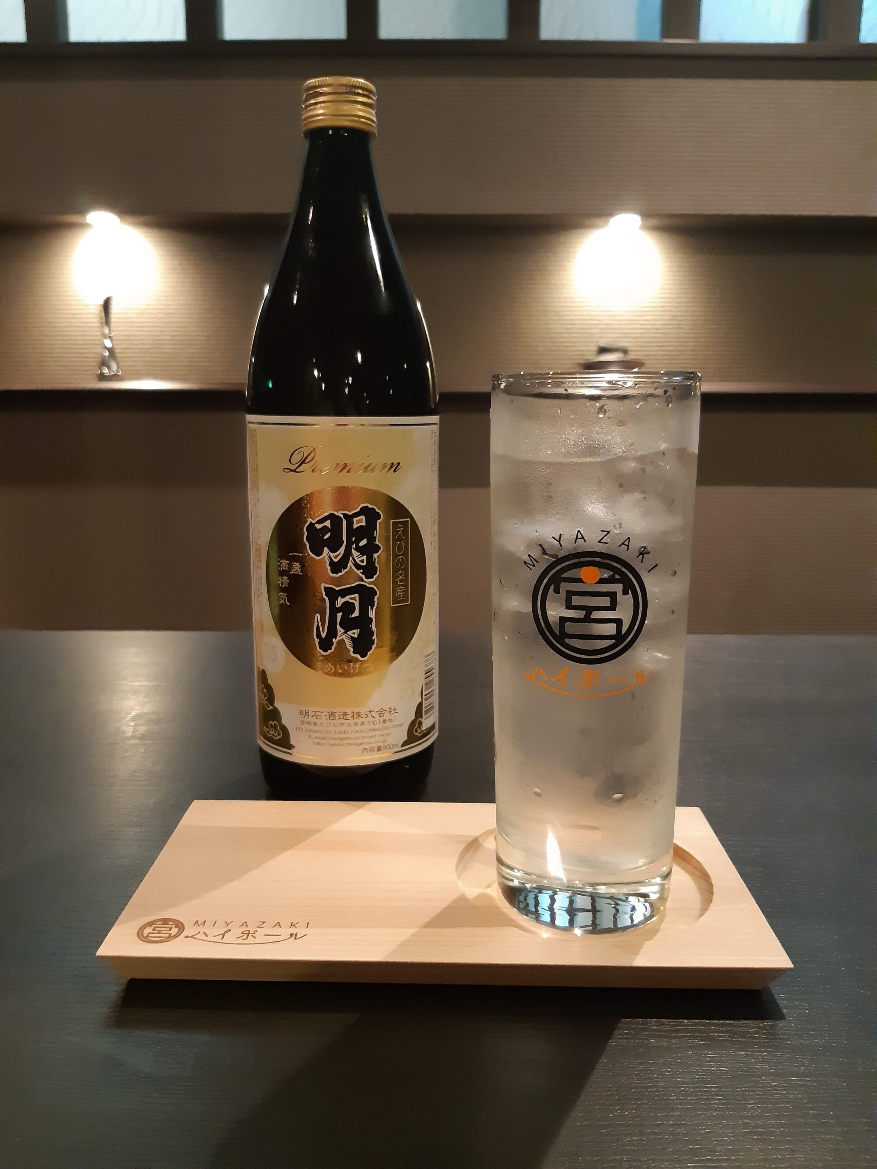 A bottle and a glass on a wooden coaster.
