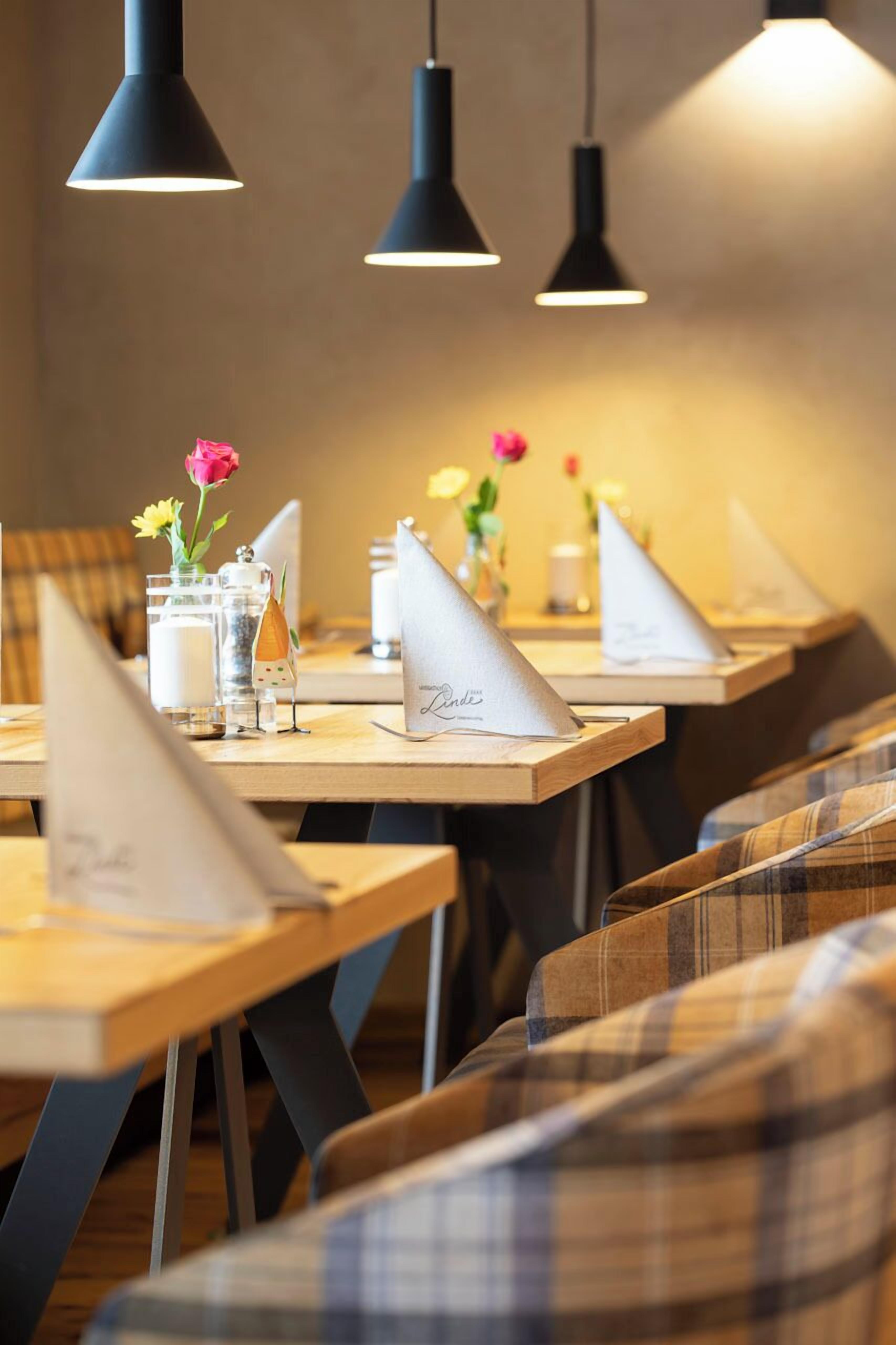 Un restaurante con mesas de madera, lámparas colgantes negras y centros de mesa con flores.