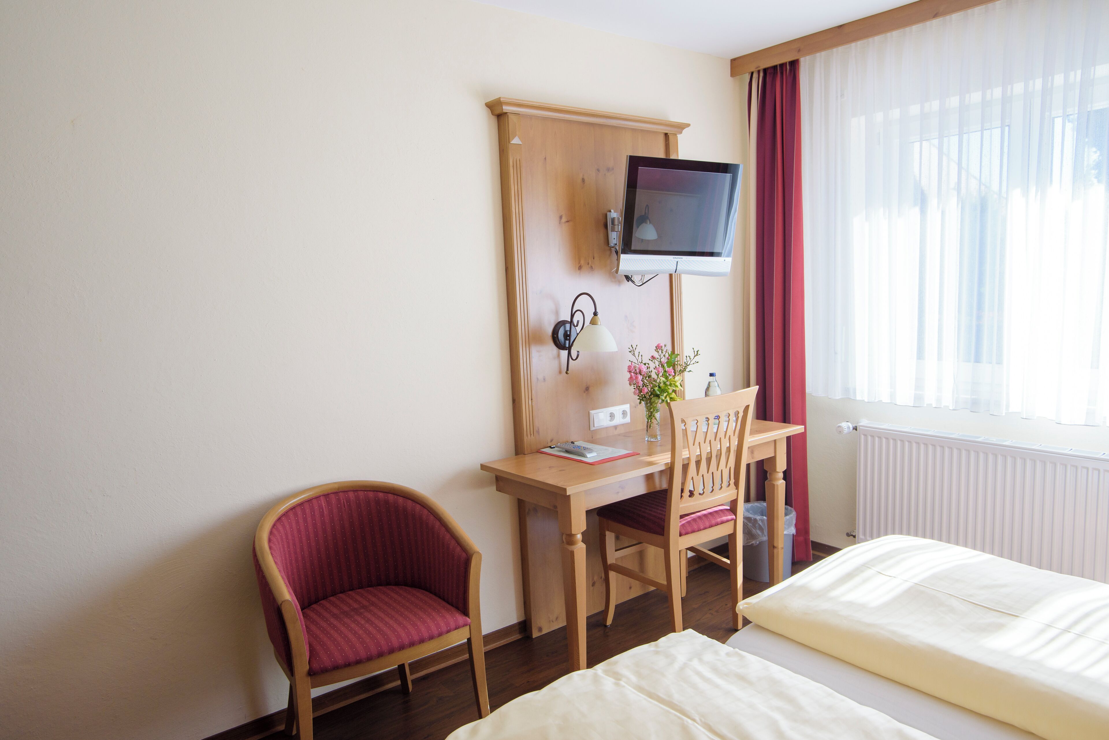 Ein Hotelzimmer mit Bett, Schreibtisch mit Stuhl, Wandfernseher und einem Vorhangfenster.