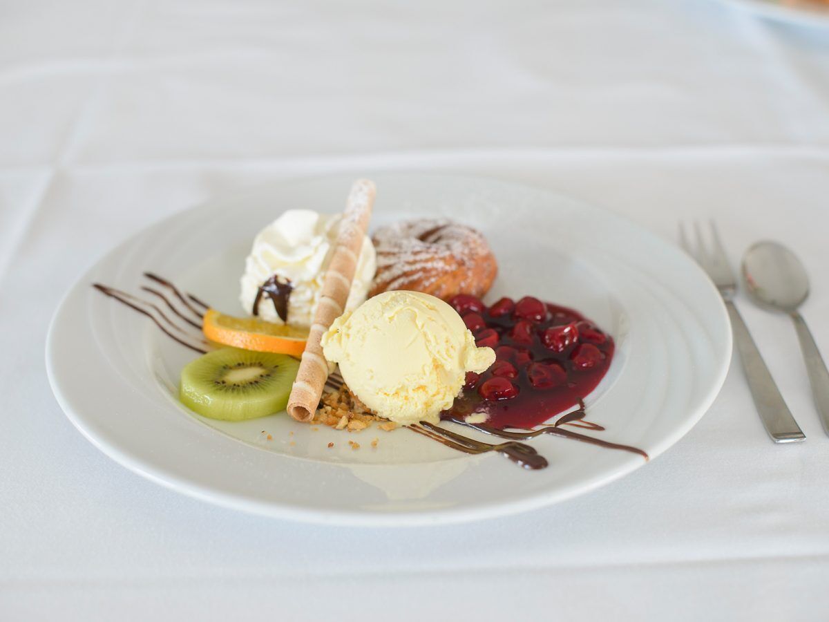 Ein Dessertteller mit Eis, Obst und einem Gebäck auf einer weißen Tischdecke.