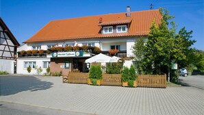 A traditional building with a tiled roof, a signboard, and a wooden fence with potted plants. - Hotel Landgasthof Linde (Deggenhausertal)
