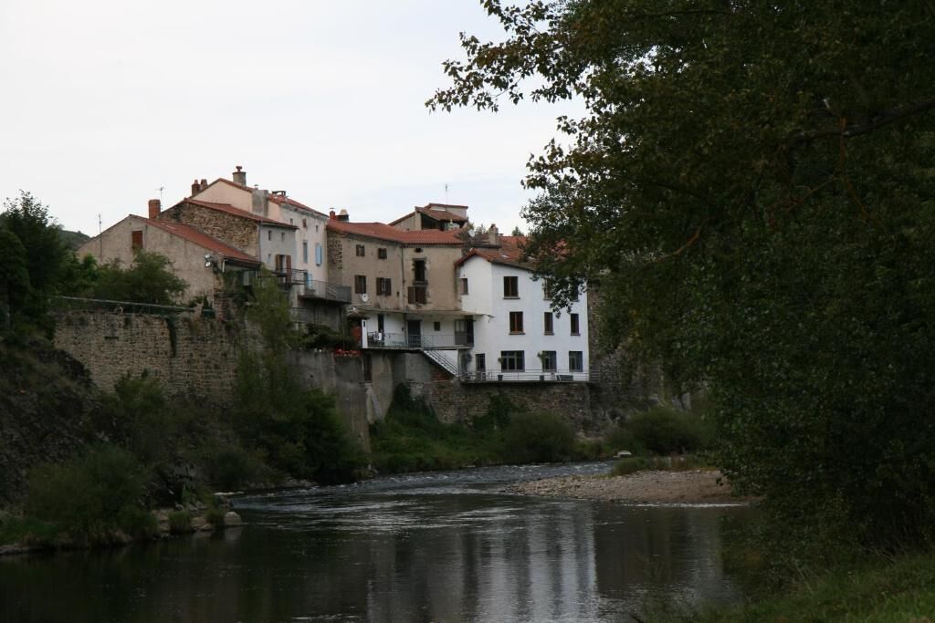 Ein mehrstöckiges Gebäude am Flussufer, mit einer Steinmauer und einer Brücke, die zum Gebäude führt.