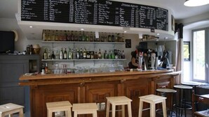 Zona de bar con un panel de menú, estantes llenos de botellas de licor, vasos y taburetes.