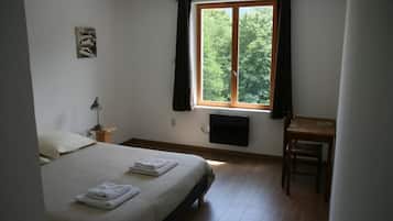 Ein Schlafzimmer mit einem Bett, einem Schreibtisch, einem Sessel, einem Fenster mit Vorhängen, einem am Wand befestigten Fernseher und einem kleinen Bild.