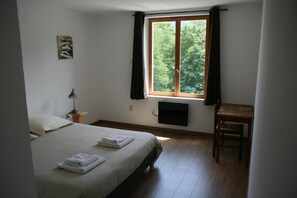 Une chambre à coucher comprenant un lit, un bureau, une chaise, une fenêtre avec des rideaux, un téléviseur fixé au mur et un petit tableau accroché au mur.