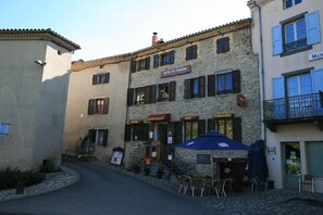 Un bâtiment avec une enseigne indiquant « Hôtel du Pêcheur » et « Restaurant ». On y trouve des tables et des chaises à l’extérieur, ainsi qu’un parasol bleu.