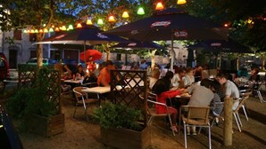 Un área de comedor al aire libre con mesas y sillas, sombrillas y luces colgantes.