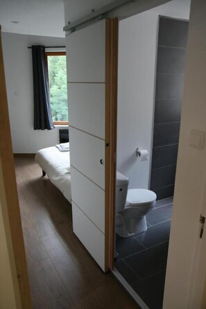 Une chambre moderne avec un lit, une salle de bain avec des toilettes et une douche, et une porte coulissante donnant sur une autre pièce.