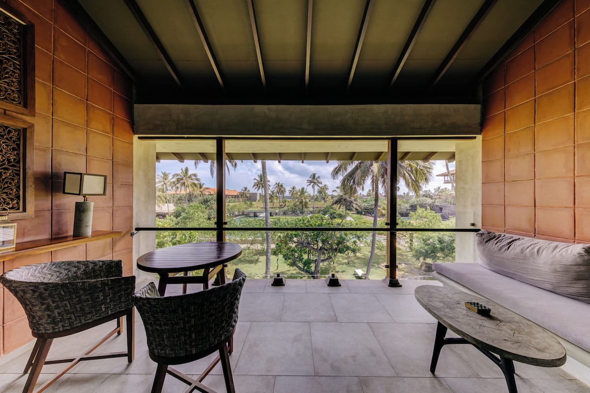 Un balcón con sofá, dos sillones, una mesita y vistas a palmeras y un paisaje lejano.