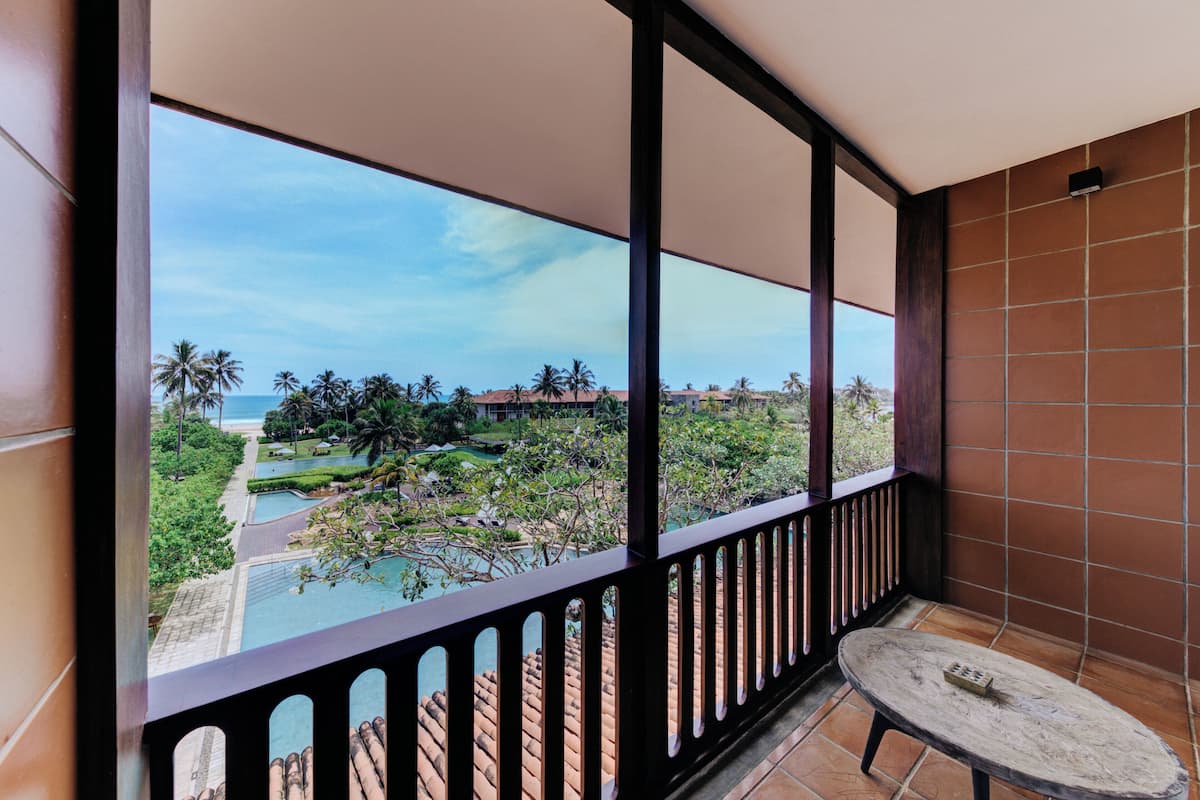 Un balcón con vista a una piscina, palmeras y un edificio lejano.